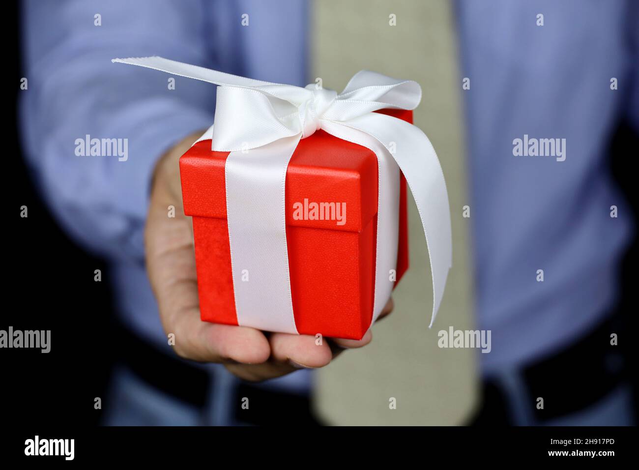 Rote Geschenkbox in männlichen Händen Nahaufnahme. Mann in Bürokleidung gibt Geschenk mit weißem Band, Konzept von Weihnachten, Geburtstag oder Valentinstag Stockfoto
