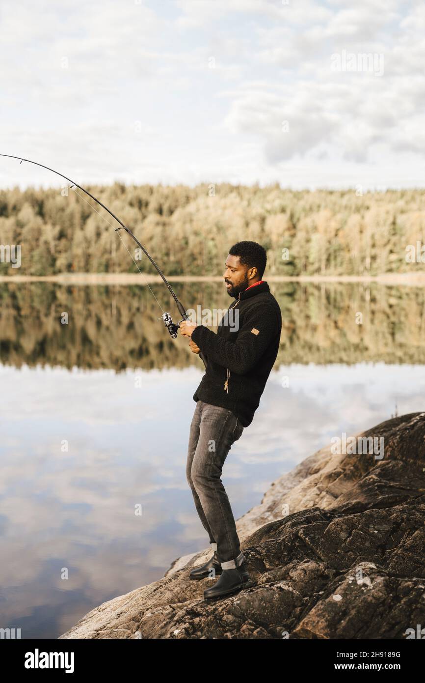 Seitenansicht des Fischers, während er auf einem Felsen steht Stockfoto