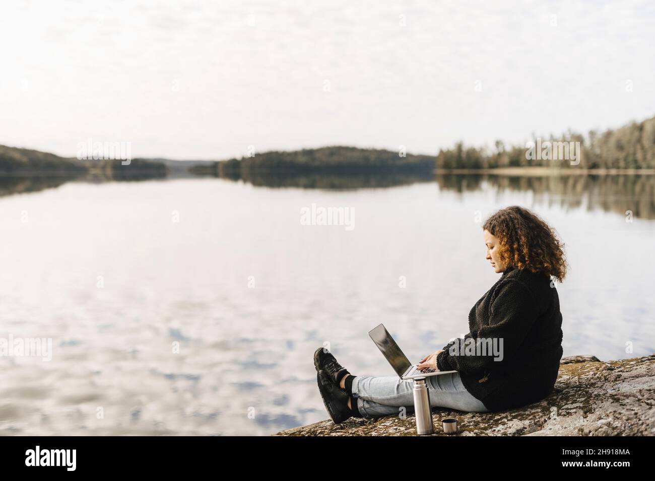 Frau, die am Wochenende an einem Laptop am Seeufer arbeitete Stockfoto