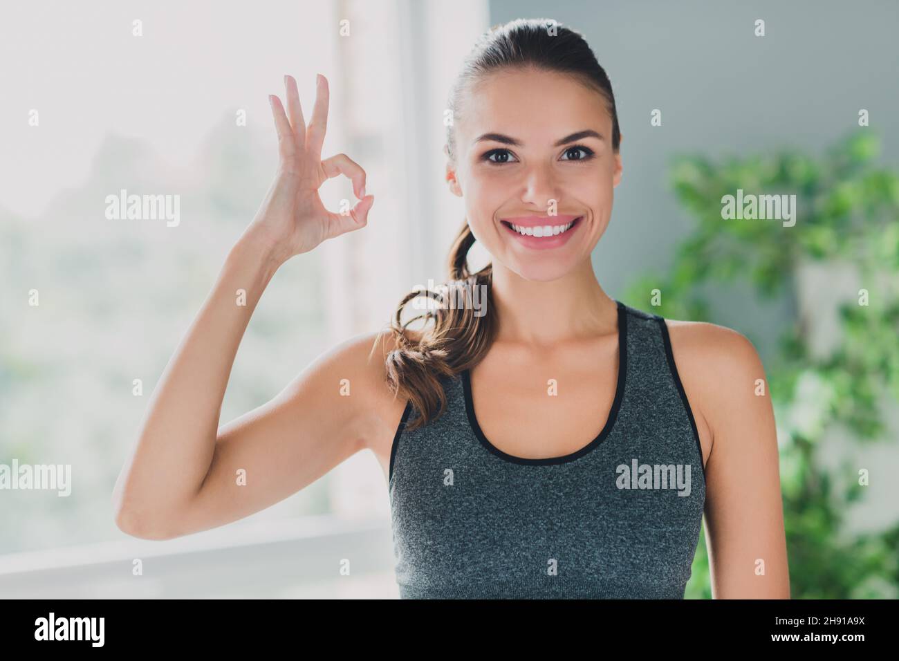 Foto von niedlichen charmanten junge Dame tragen Sport-Outfit lächelnd zeigt okey Zeichen im Haus Haus Stockfoto