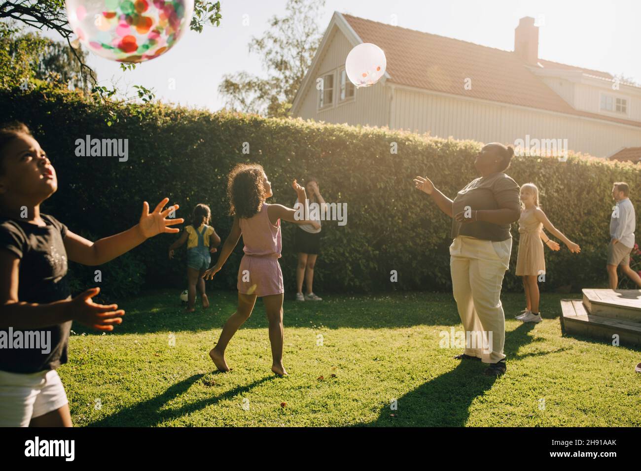 Frau und Kinder, die an sonnigen Tagen im Garten mit Ballons spielen Stockfoto