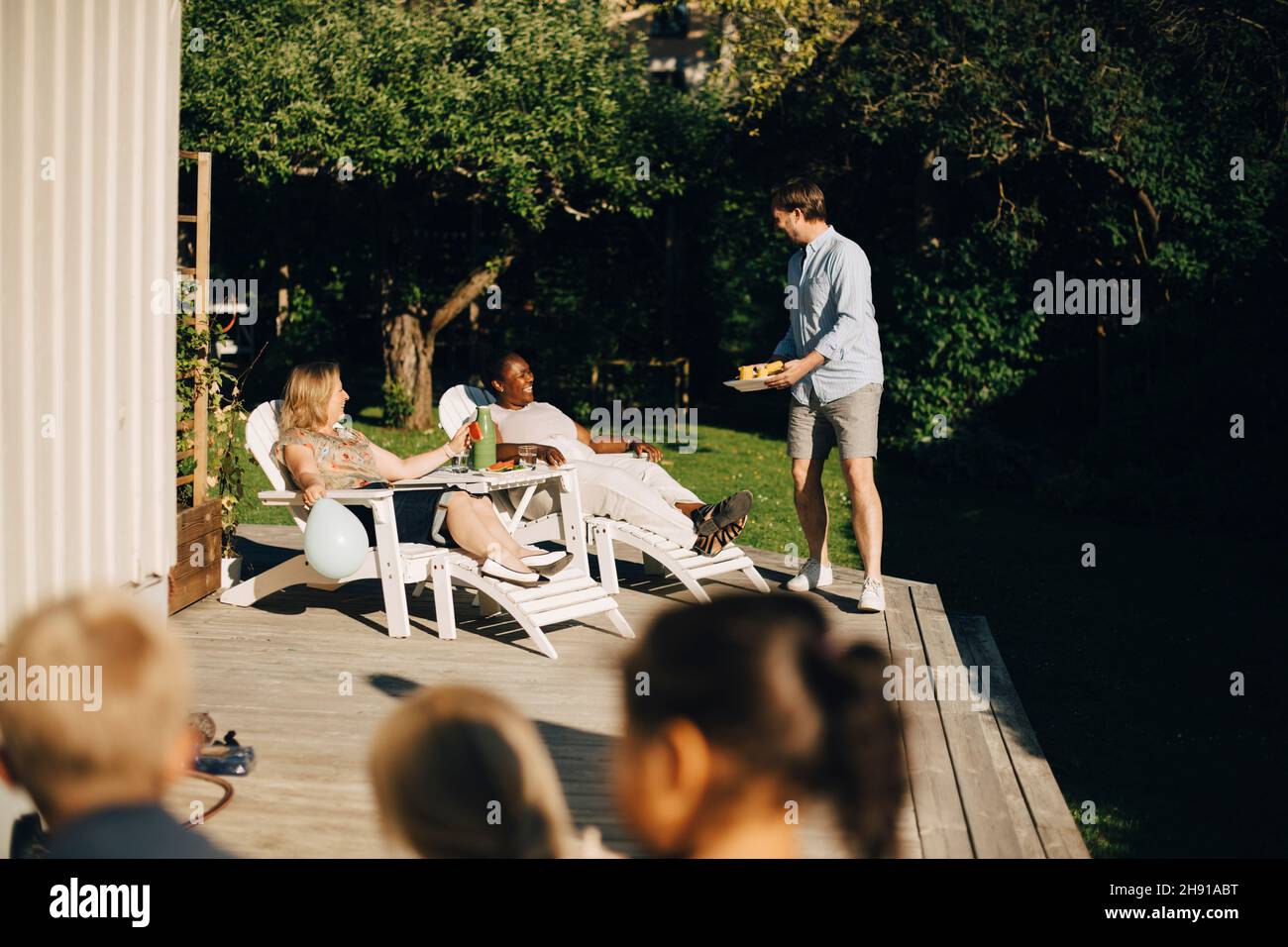 Mann, der Frauen während einer Gartenparty auf der Terrasse Essen servierte Stockfoto