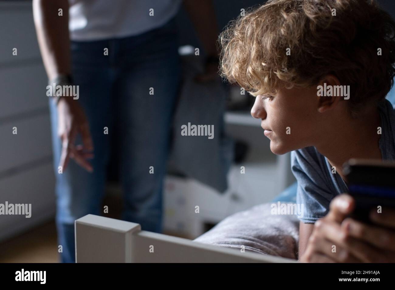 Junge mit Mobiltelefon, das von der Mutter im Schlafzimmer auf dem Bett liegt Stockfoto