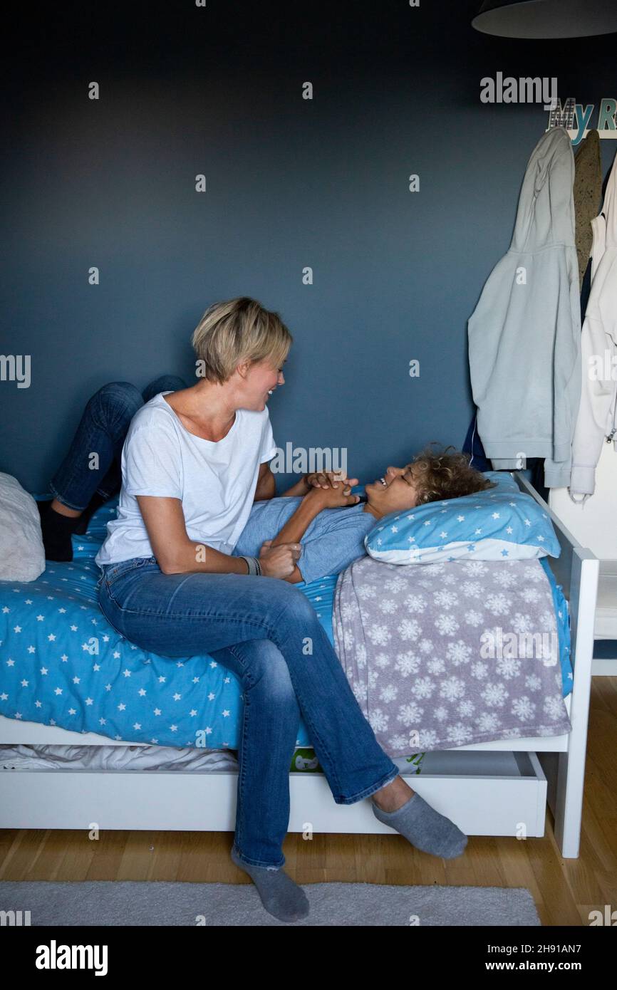 Lächelnde Mutter, die mit dem Sohn spricht, während sie im Schlafzimmer auf dem Bett sitzt Stockfoto