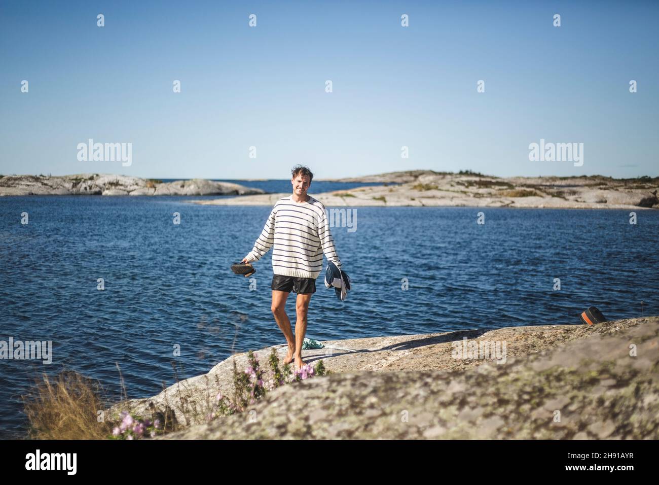 Mittelerwachsener Mann, der während der Sommerferien auf Felsen gegen das Meer steht Stockfoto