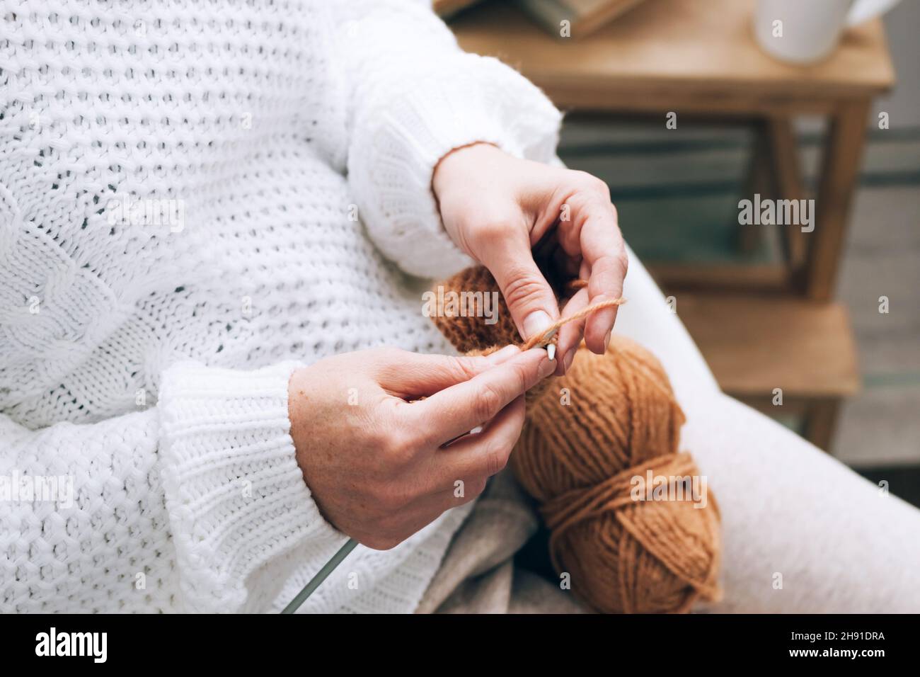 Eine Frau mittleren Alters beschäftigt sich mit häuslicher Handarbeit Stricken, Stricken mit Fäden. Home-Aktivität Hobby in der Freizeit Stockfoto