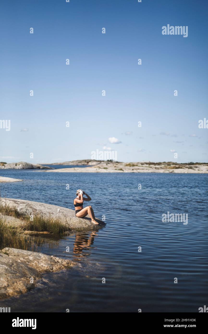 Frau, die sich an sonnigen Tagen auf Felsen am Meer Haare wäscht Stockfoto