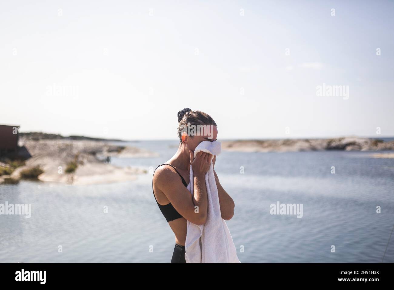 Frau, die das Gesicht mit einem Handtuch gegen das Meer putzt Stockfoto