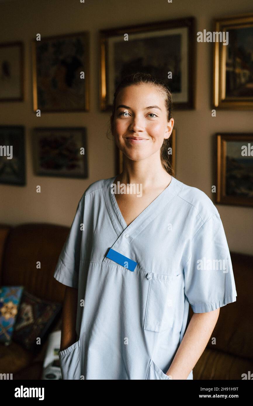 Lächelnde weibliche Pflegekraft mit Händen in den Taschen im Pflegeheim Stockfoto