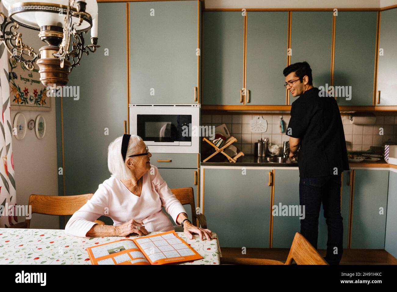 Ältere Frau im Gespräch mit einem männlichen Mitarbeiter im Gesundheitswesen, der in der Küche arbeitet Stockfoto