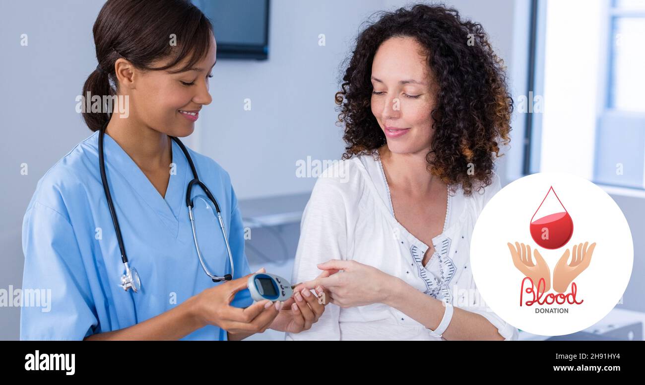 Lächelnder Arzt, der Glucometer bei einer Patientin im Krankenhaus mit Blutspendesymbol verwendet Stockfoto