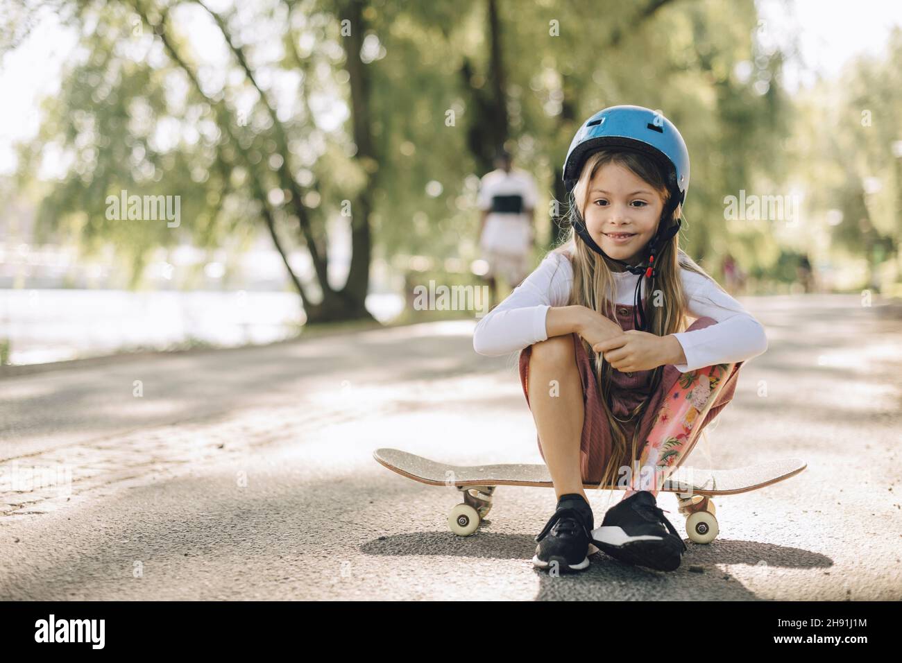 Mädchen mit Beinprothese schaut nach unten, während sie auf dem Skateboard im Park sitzt Stockfoto