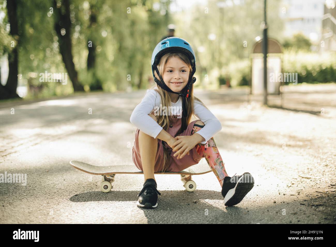 Lächelndes Mädchen mit prothetischem Bein, während es auf dem Skateboard sitzt Stockfoto