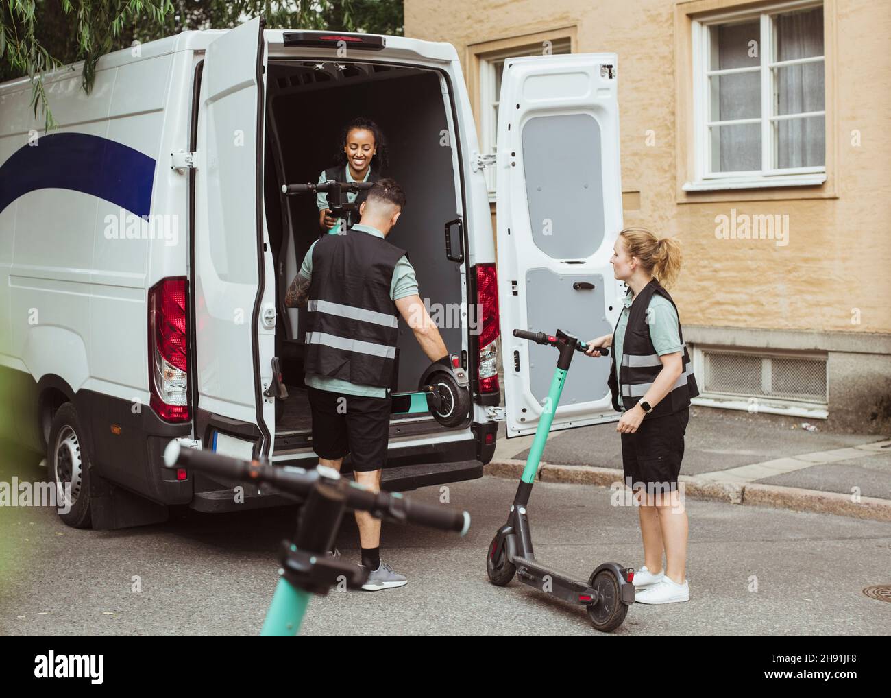 Weibliche und männliche Arbeiter laden elektrische Push-Scooter in Lieferwagen Stockfoto