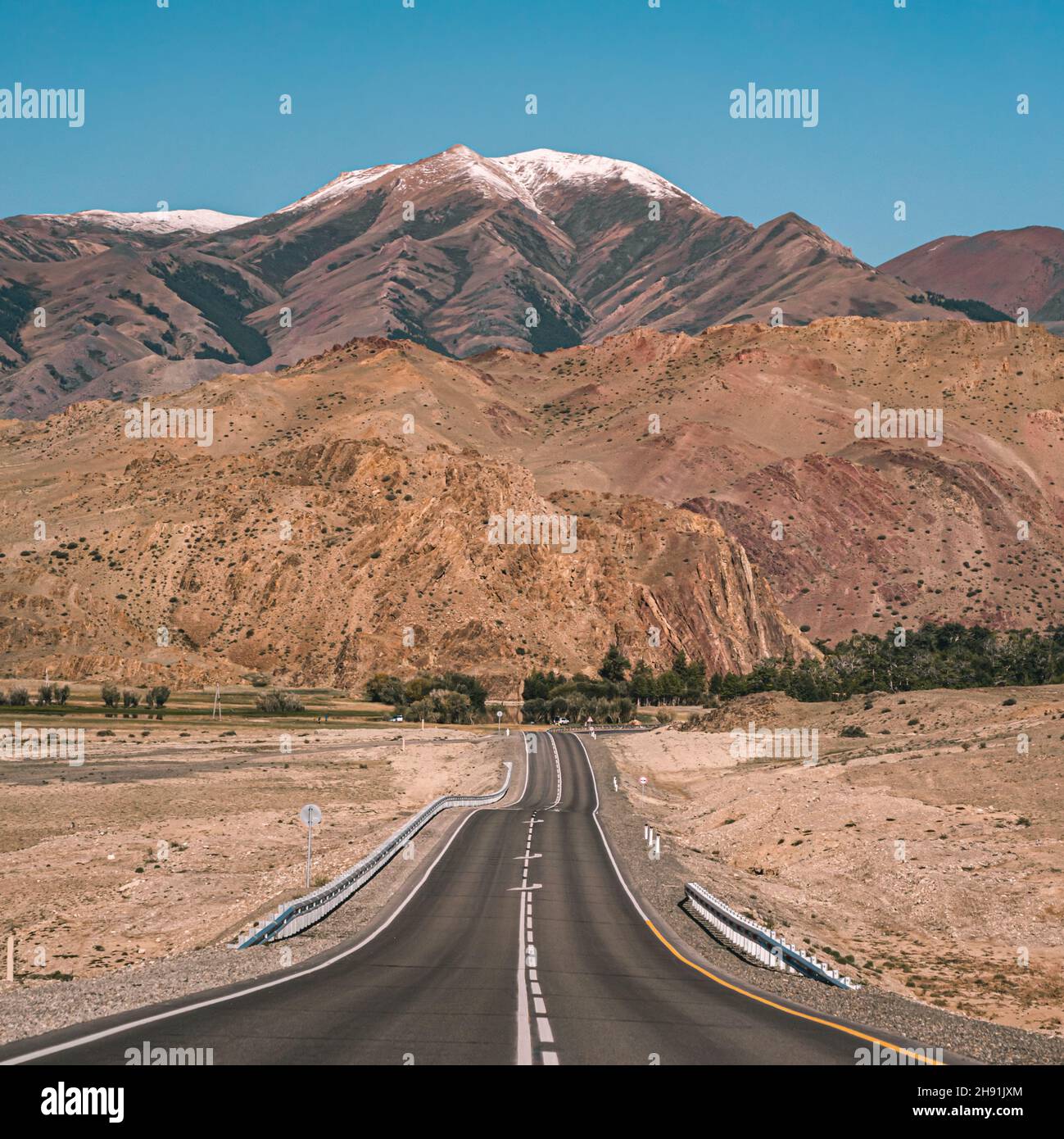 Leere Asphaltstraße vor riesigen majestätischen Bergen mit schneebedeckten Gipfeln. Schöne Landschaft der Region Altay, Russland. Stockfoto