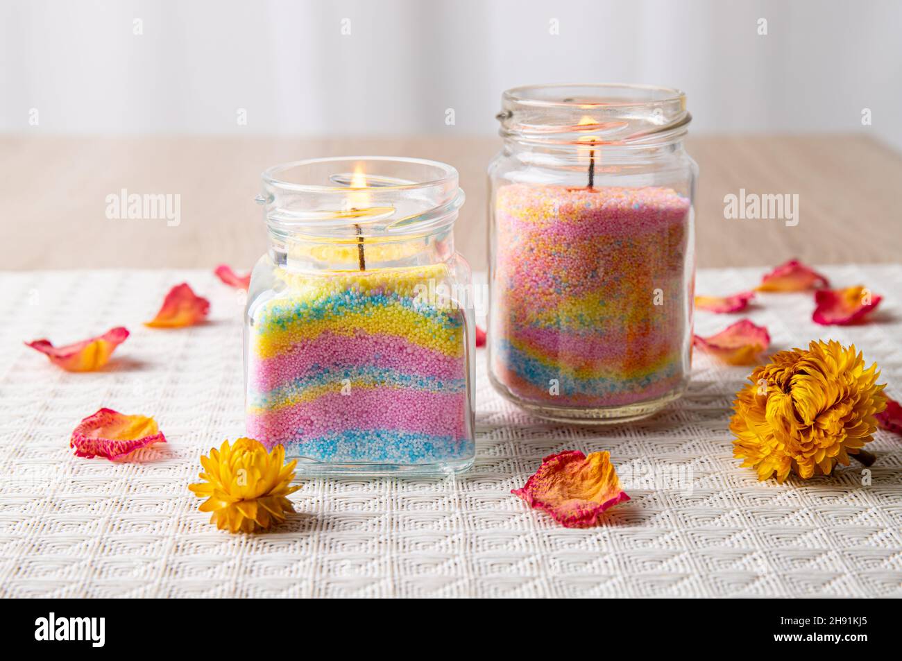 Kinder machten lustige bunte geschichtete Wachspulderkerzen in zu Hause, indem sie Pulver in alte Babynahrung eingossen und Docht innen einsetzten, minimaler Hintergrund. Stockfoto