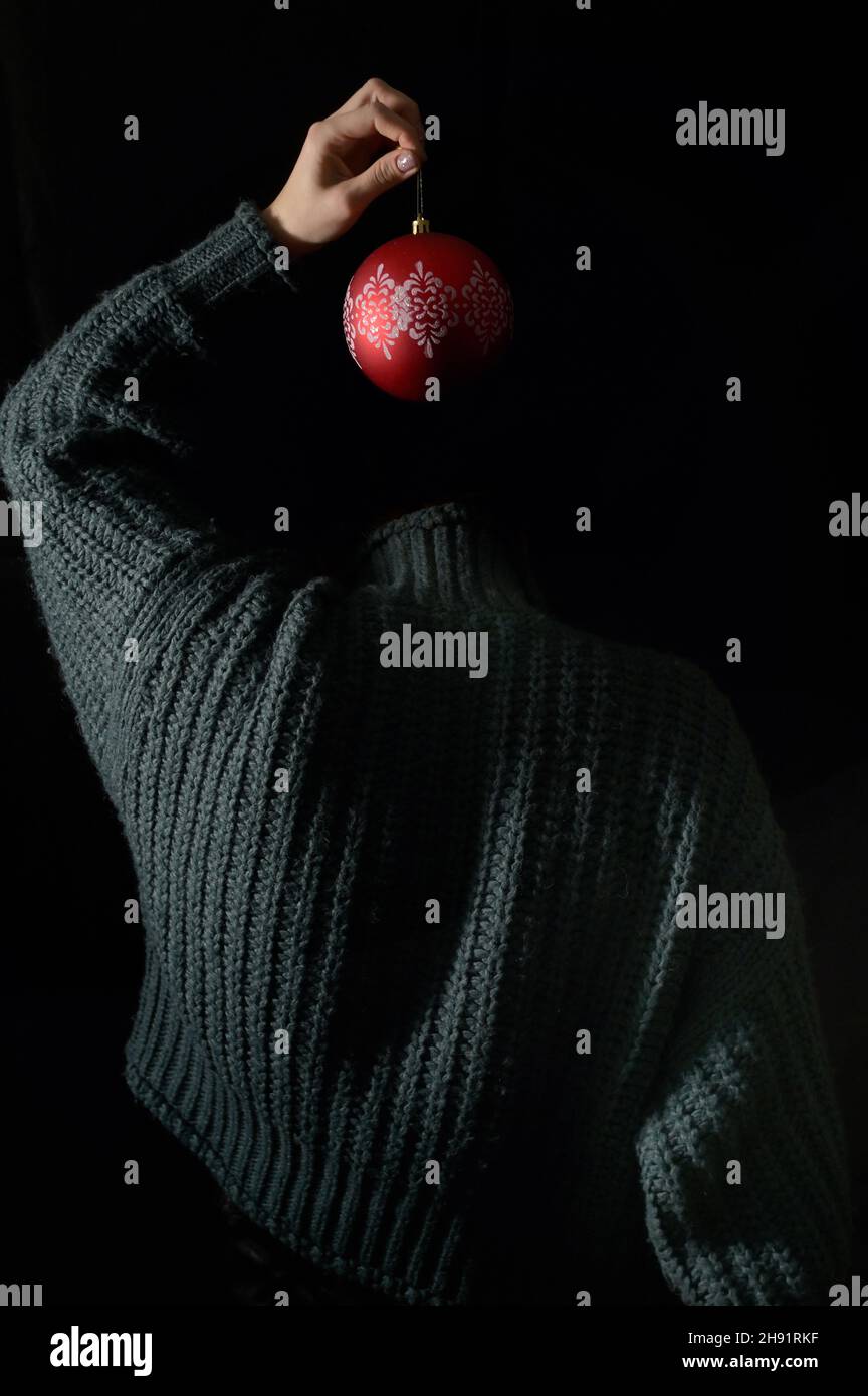 Die Hand einer verborgenen Frau hängt einen Weihnachtsball mit Ornament Stockfoto