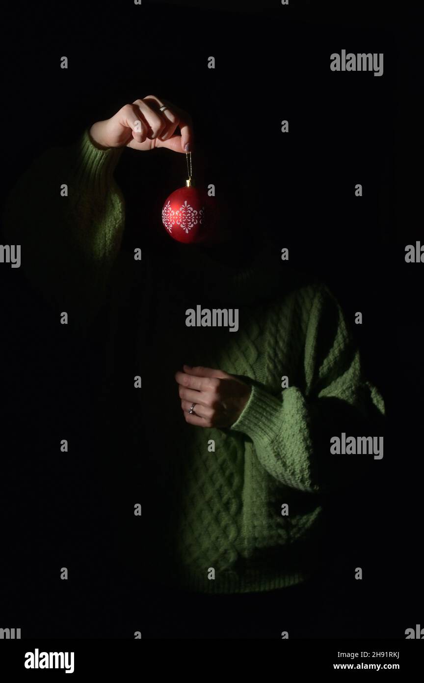 Die Hand einer verborgenen Frau hängt einen Weihnachtsball mit Ornament Stockfoto