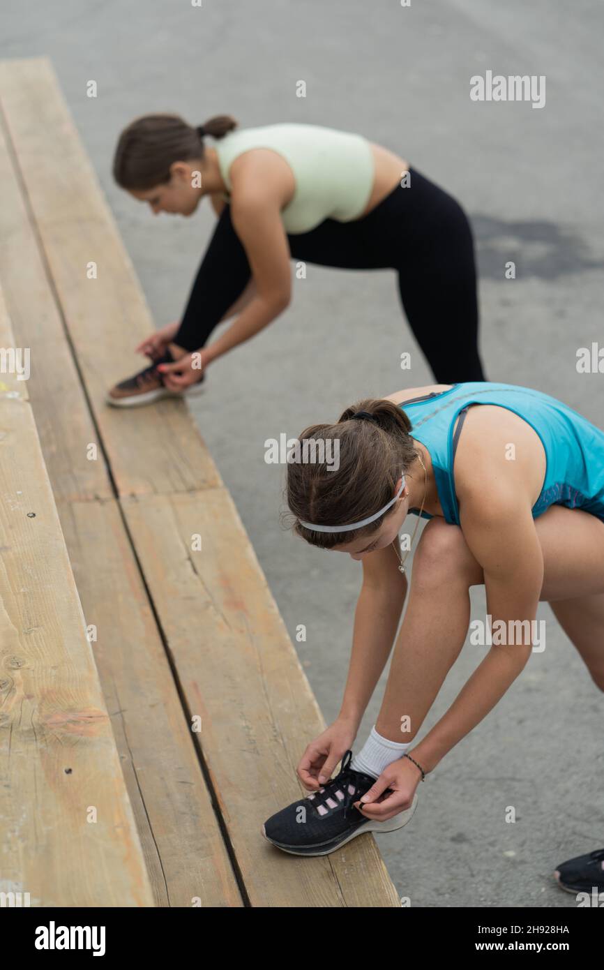 Zwei Mädchen knieen ihre Schnürsenkel vor ihrer Dehnungsroutine draußen Stockfoto