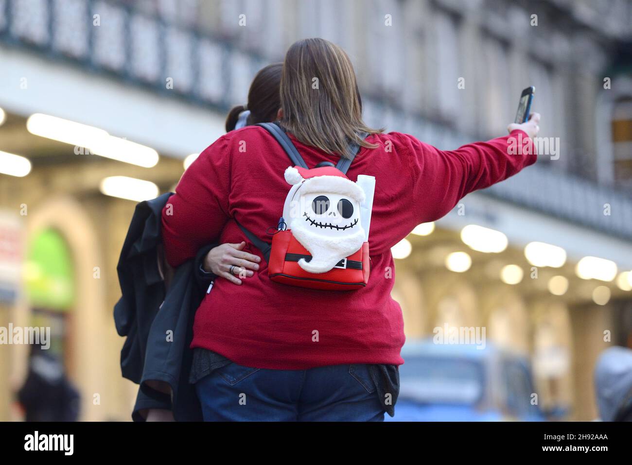 London, England, Großbritannien. Zwei junge Frauen, die ein Selfie mit einem Jack Skellington Nightmare before Christas Rucksack machen, Dezember 2021 Stockfoto
