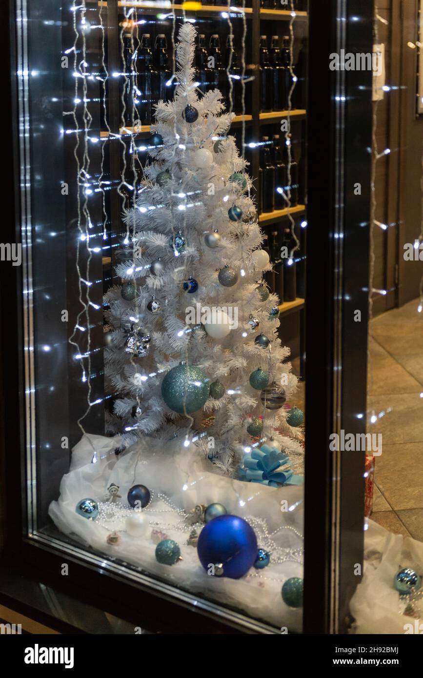 Weißer Weihnachtsbaum hinter Glas. Stilvoller künstlicher Weihnachtsbaum mit blauen und blauen Kugeln. Das Schaufenster des neuen Jahres Stockfotografie