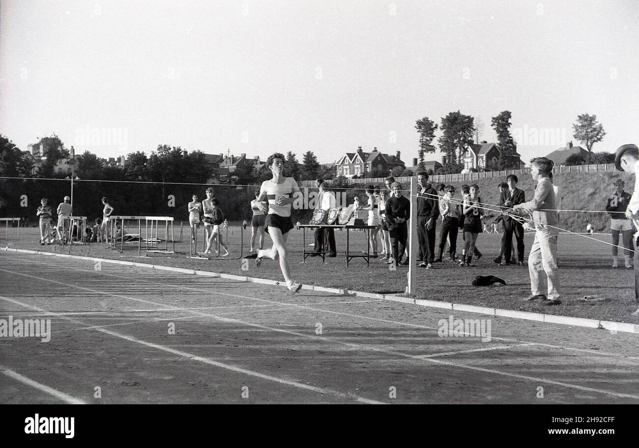 1964, historisch, im Sommer und an einem Sporttag an einer Bezirksschule auf einer Schlackenlaufbahn, traf ein Schüler der sechsten Schulklasse am Ende eines Rennens das Zielband, Devon, England, Großbritannien. Stockfoto