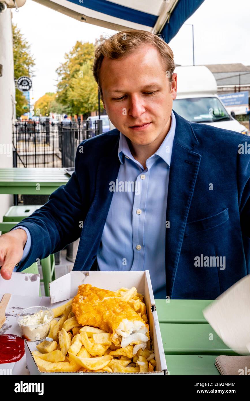 Ein gut gekleideter junger Mann, der eine Fish and Chip-Mahlzeit isst, London, Großbritannien. Stockfoto