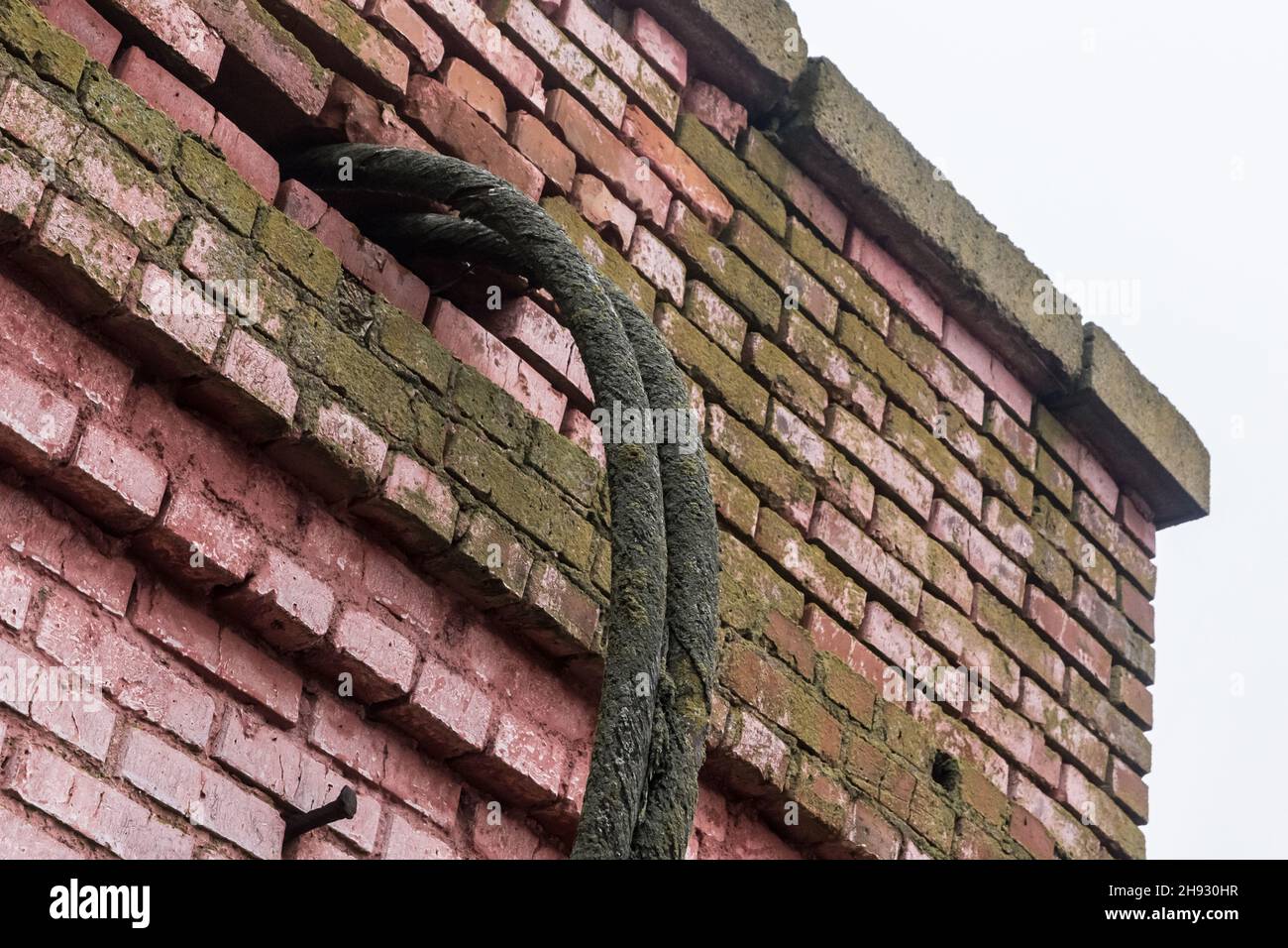 Ein alter, schmutziger Elektrokabeldraht in der Ziegelwand der Fassade eines verlassenen Hauses. Stockfoto