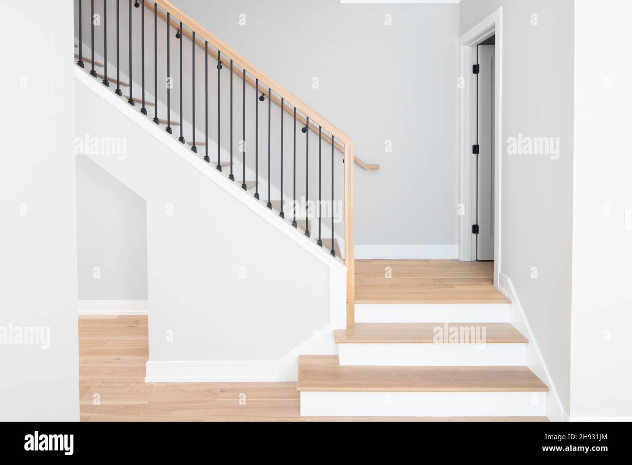 Eine Treppe mit Stufen und Handläufen aus natürlichem Holz, weißen Steigleitungen und schmiedeeisernen Spindeln. Stockfoto