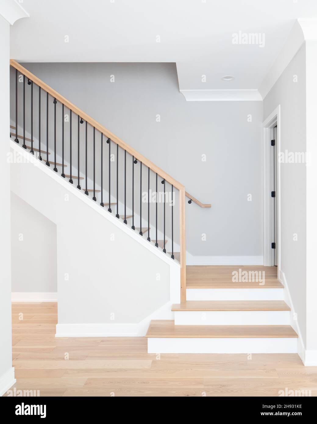 Eine Treppe mit Stufen und Handläufen aus natürlichem Holz, weißen Steigleitungen und schmiedeeisernen Spindeln. Stockfoto