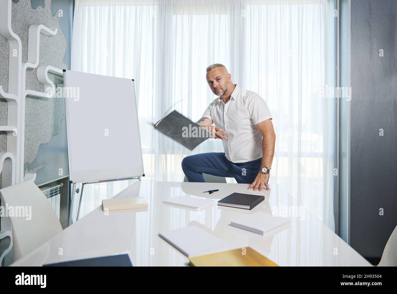 Schöner Mann aus dem mittleren Alter, erfolgreicher Unternehmer, Psychologe, der neben einem Flipchart mit Platz für Text steht und ein b wirft Stockfoto