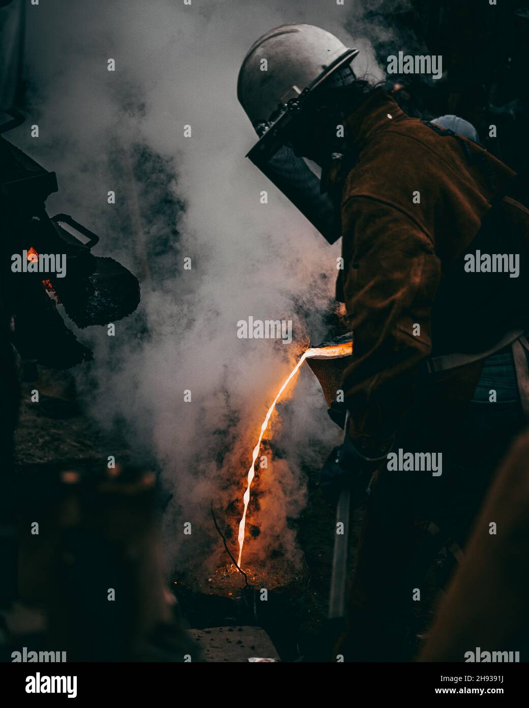 Vertikale Aufnahme eines erwachsenen Industriearbeiters in Uniformen, der in einer Fabrik Metall schmelzt Stockfoto