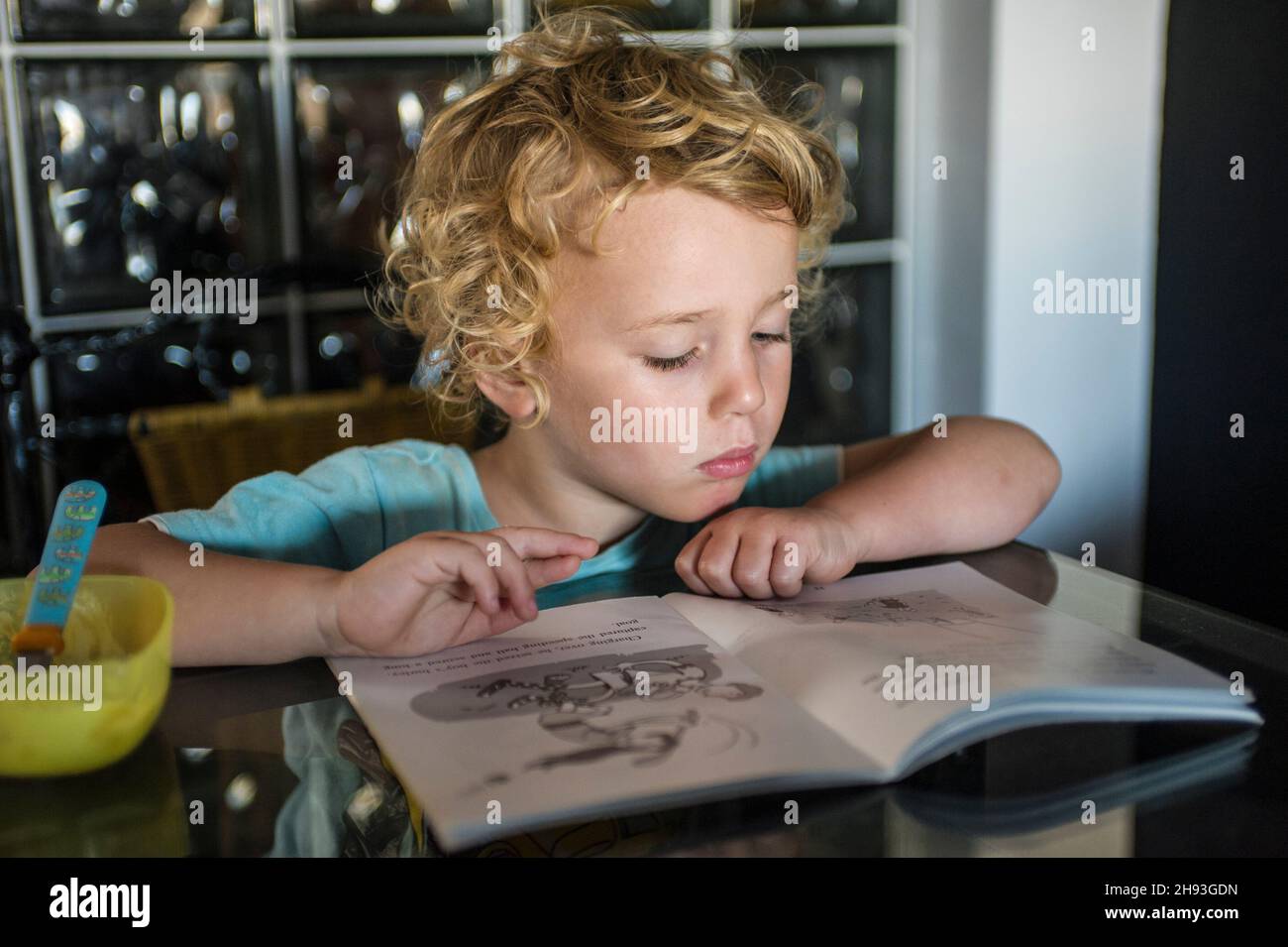 Ein kleiner Junge (3 Jahre alt) liest ein Buch an einem Tisch in seinem Haus. Stockfoto