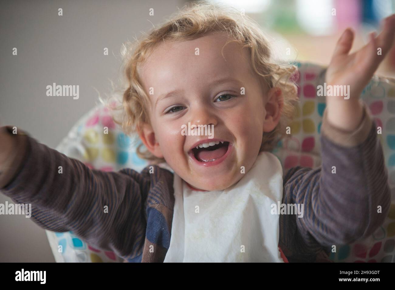 Ein 2-jähriges Baby lacht und jubelt, während sie auf einem Hochstuhl sitzt. Stockfoto