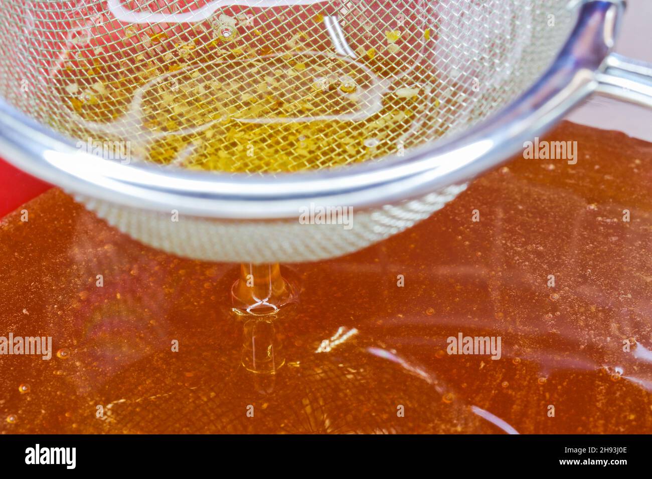 Golden Raw Honey fließt durch die Siebe Close-Up Stockfoto