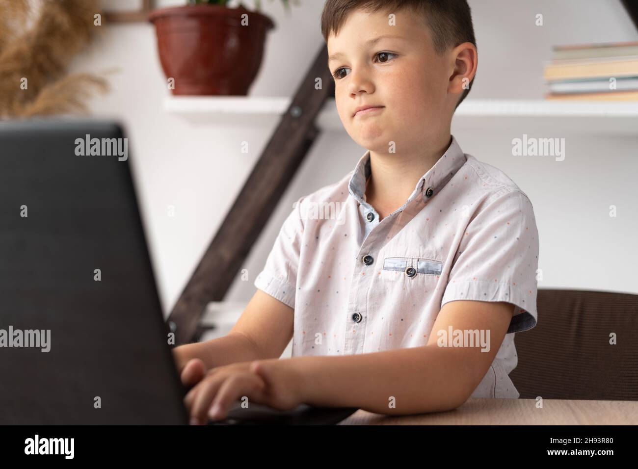 Porträt eines konzentrierten Schuljungen, der zu Hause auf der Tastatur eines Laptops tippt oder ein virtuelles Computerspiel spielt. Motivierter Student beim Studieren Stockfoto