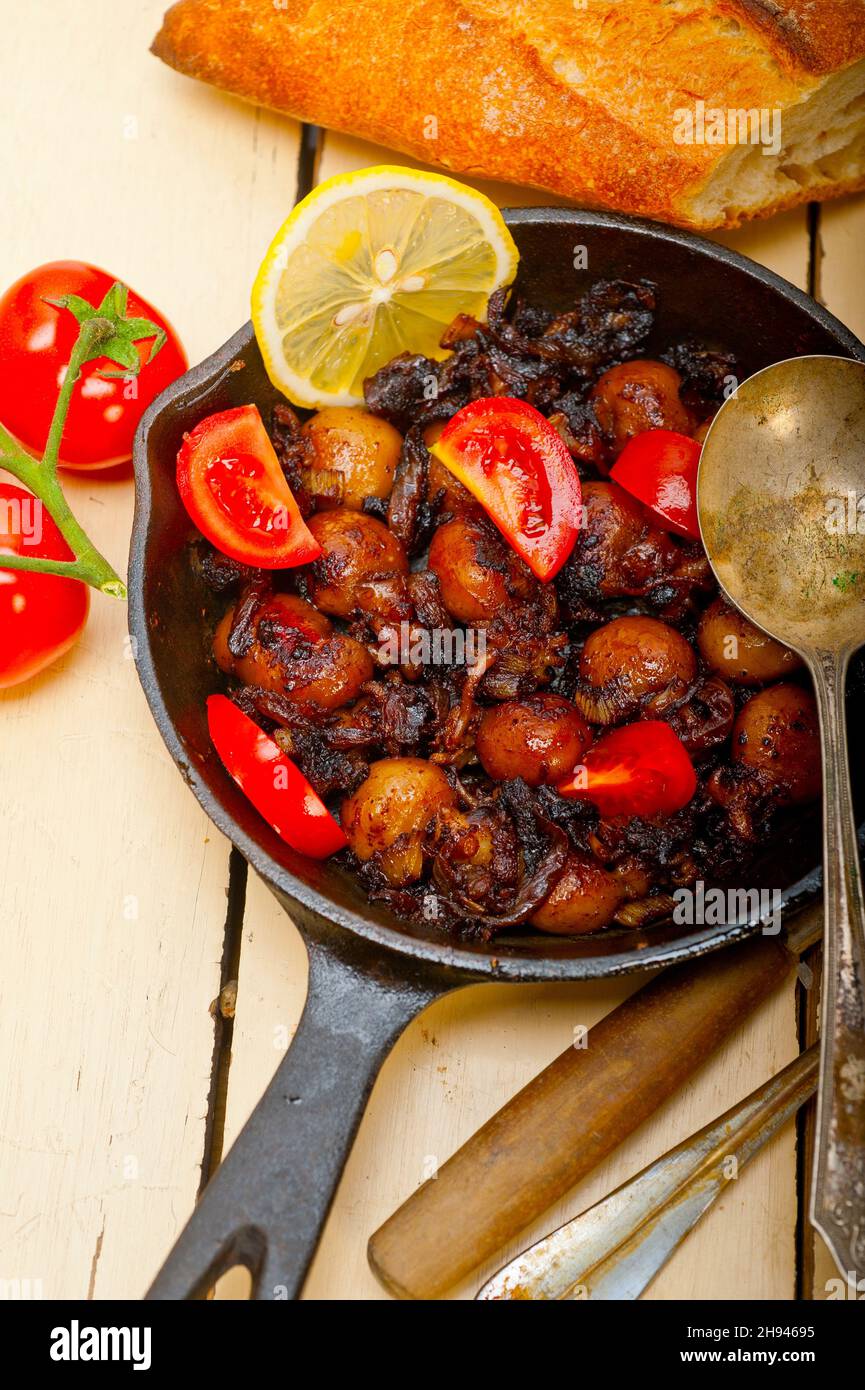 Baby Tintenfisch über rustikalen Holztisch auf eisernen Pfanne mit Tomaten und Zwiebeln gebraten Stockfoto