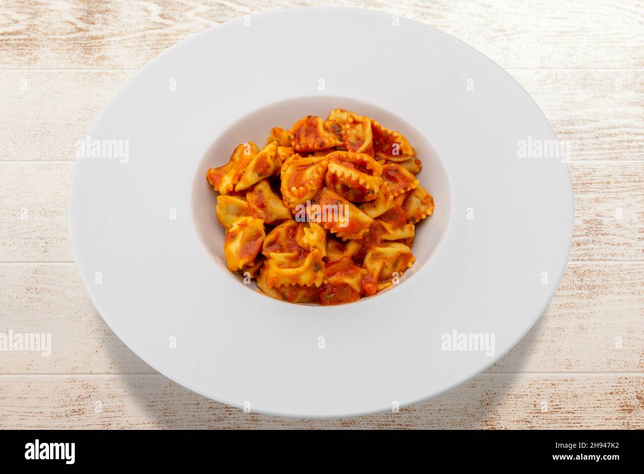 Typische Agnolotti del plin, gefüllte Eiernudelravioli aus Langhe, Piemont, Italien, gewürzt mit Tomatensauce in weißer Schale auf Holztisch Stockfoto