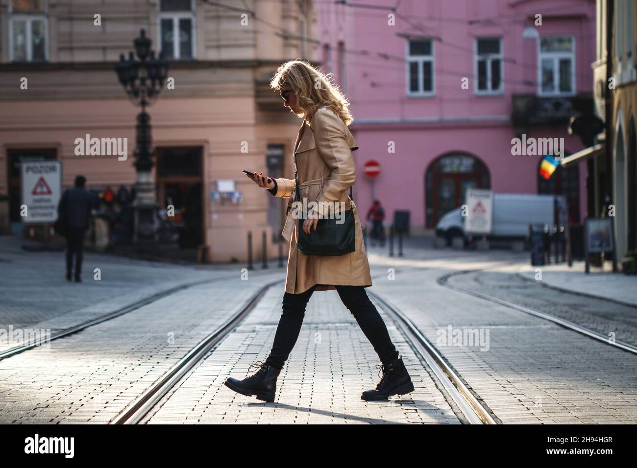 Seien Sie vorsichtig, wenn Sie die Straße überqueren. Frau, die in der Stadt herumläuft, während sie SMS auf ihrem Mobiltelefon liest. Abgelenkte und unachtsame Menschen unterwegs Stockfoto