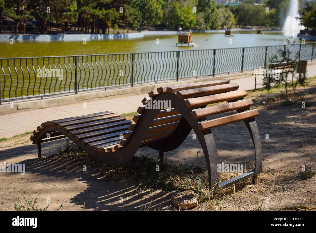 Eine geschwungene, gebogene Holzdekorbank aus Brettern steht in einem Sommerpark leer Stockfoto