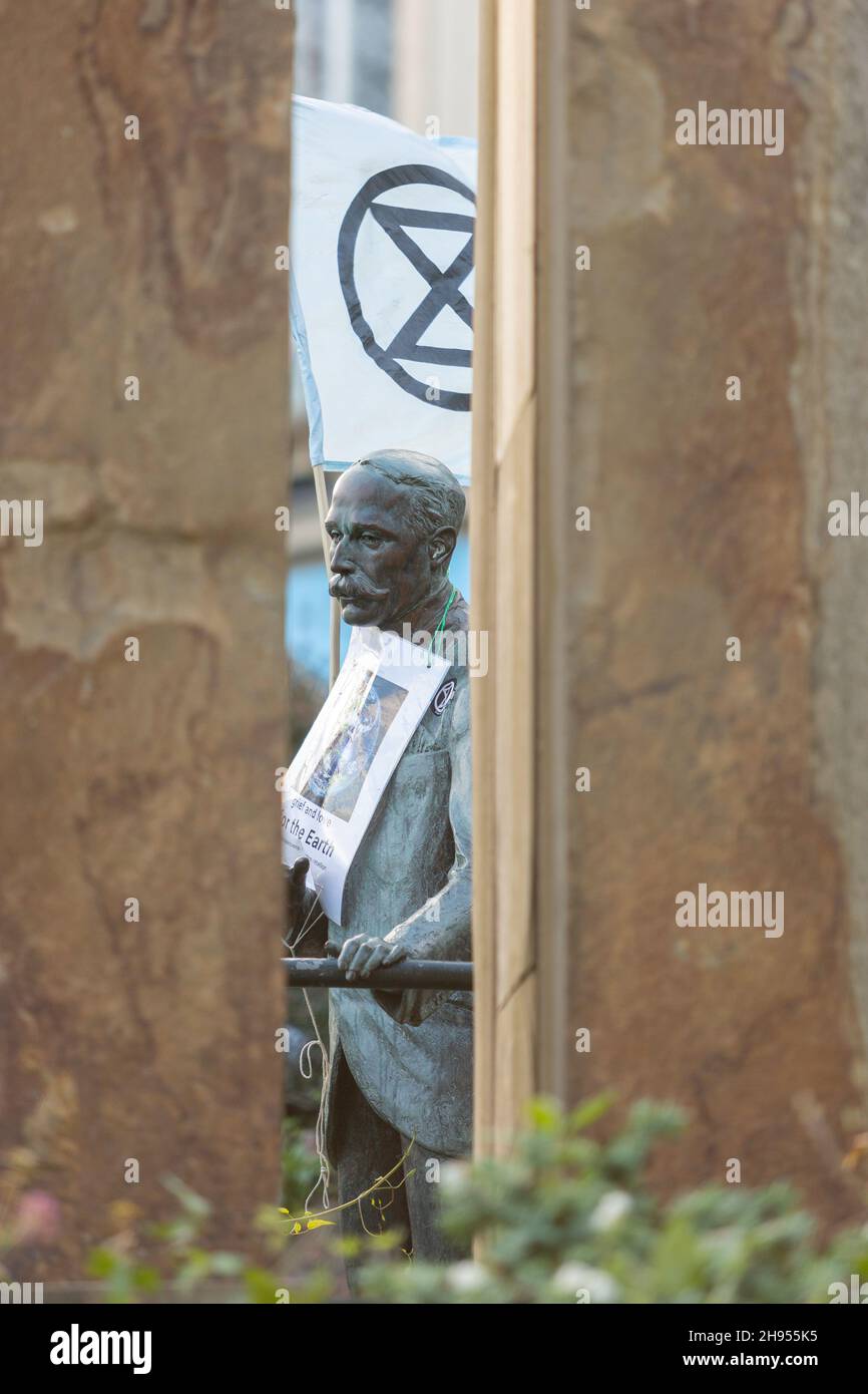 Great Malvern, Worcestershire, Großbritannien. 4th Dez 2021. An der Bronzestatue von Sir Edward Elgar auf der Bell Vue Terrace Island, Great Malvern, Worcestershire, ist eine Flagge der Rebellion des Aussterbens angebracht. Der berühmte englische Komponist ist ein unwissensvoller Unterstützer der Klimaaktivisten, die XR Malvern anstrebt, da seine Statue die XR-Flagge und ein Plakat mit der Aufschrift "Trauer und Liebe zur Erde" trägt. Kredit: Peter Lopeman/Alamy Live Nachrichten Stockfoto