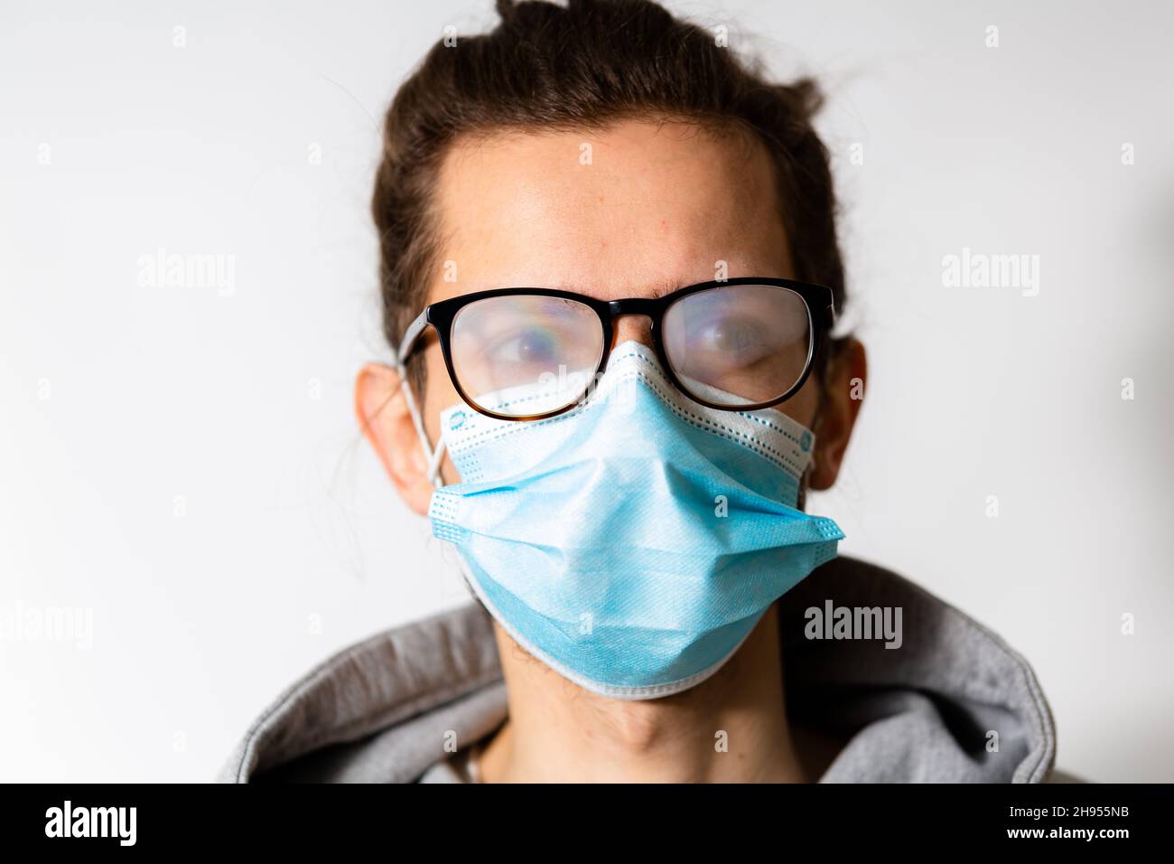 Junger Mann mit nebligen Gläsern durch das Tragen von Einwegmaske verursacht. Schutzmaßnahme während einer Coronavirus-Pandemie Stockfoto