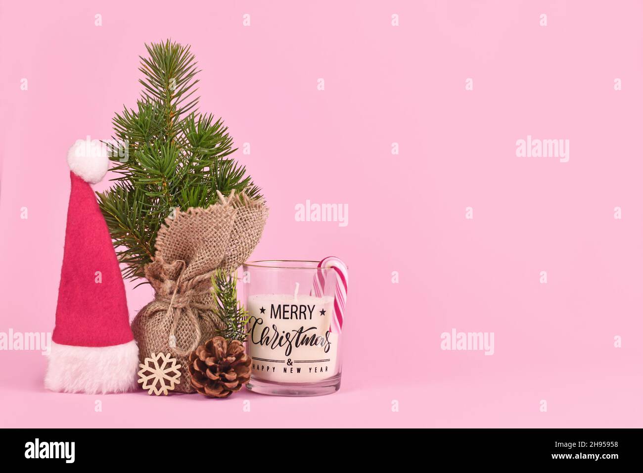Weihnachtsarrangement mit weihnachtsmütze, kleinem Baum und Kerze auf rosa Hintergrund mit Kopierraum Stockfoto