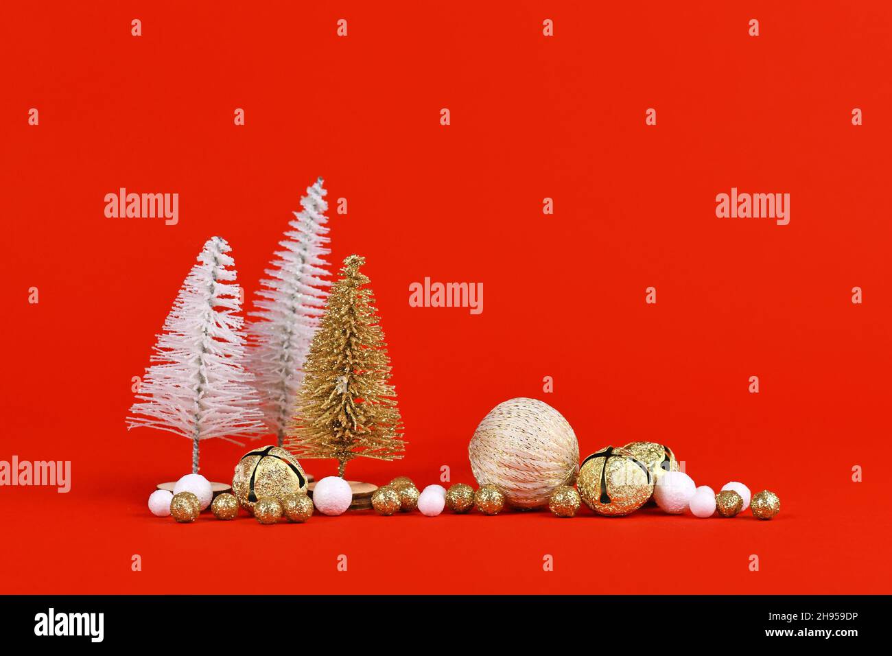 Goldene und weiße Miniaturkiefern neben weihnachtsbaumkugeln auf rotem Hintergrund Stockfoto