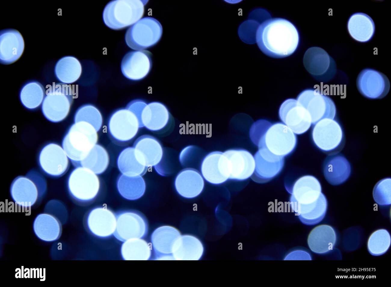 Kaltes Licht. Unschärfe Bokeh weihnachten große blaue Lichter auf schwarzem Hintergrund. Abstrakt verschwommene blaue Glitzer-Textur. Blaue Bokeh Glitzertapete Stockfoto