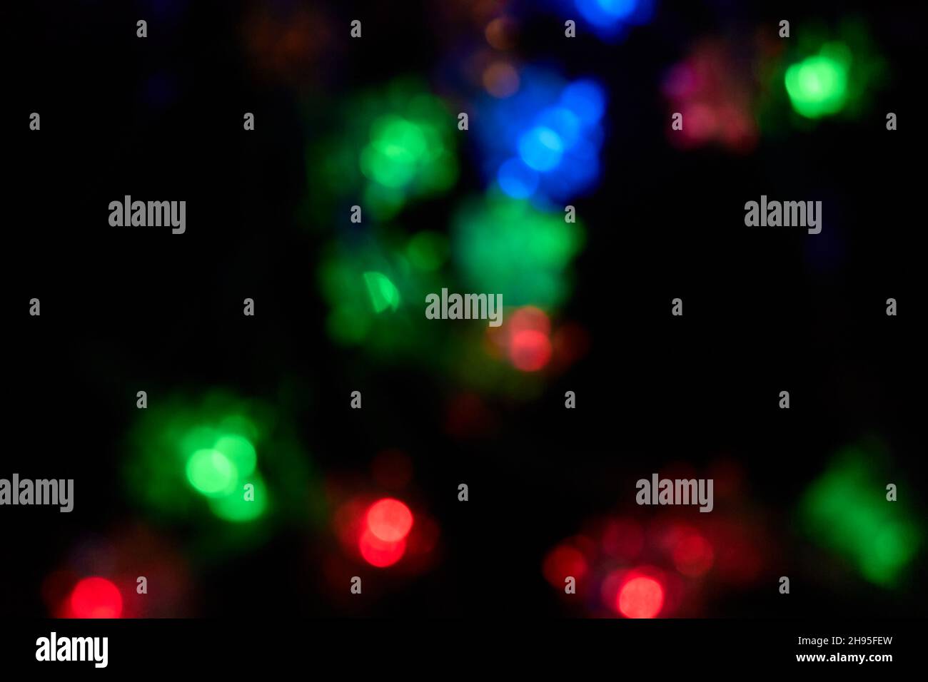 Defokussiertes Bokeh weihnachten bunte Lichter auf schwarzem Hintergrund. Verschwommene abstrakte blaue, grüne, rote Glitzerstruktur. Blur Bokeh Glitzer Tapete. Stockfoto