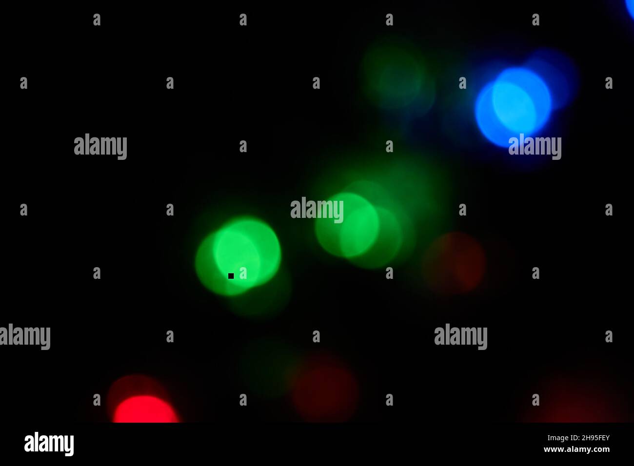 Defokussierte große Bokeh bunten Lichter auf schwarzem Hintergrund. Verschwommene abstrakte blaue, grüne, rote Flecken. Blur Bokeh Glitzer Tapete für Weihnachten Stockfoto