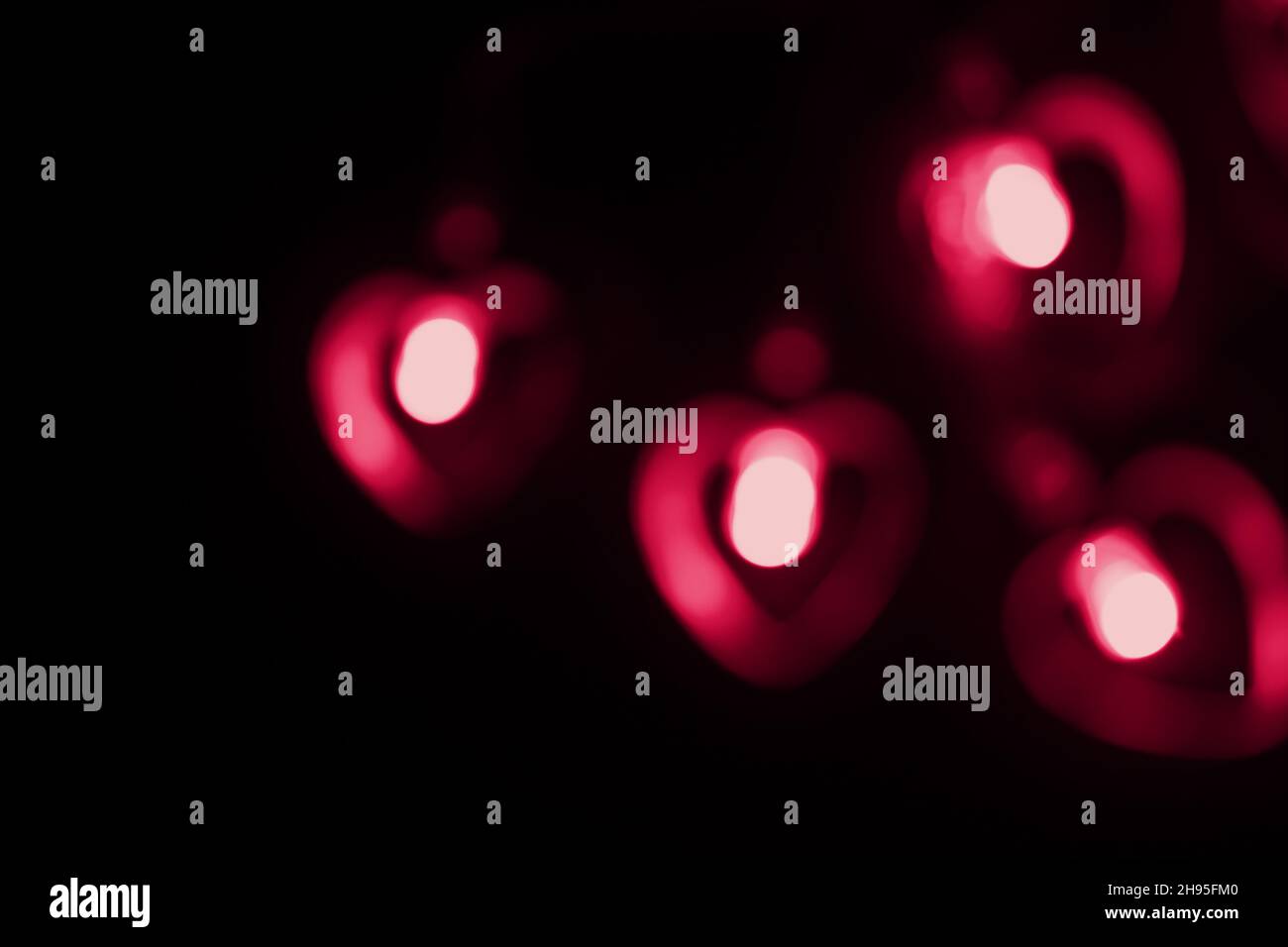 Vier große rote, verschwommene rote Lichter in Herzform auf schwarzem Hintergrund. Verschwommene abstrakte große rote Tapete für Liebe Thema, Valentinstag. Stockfoto
