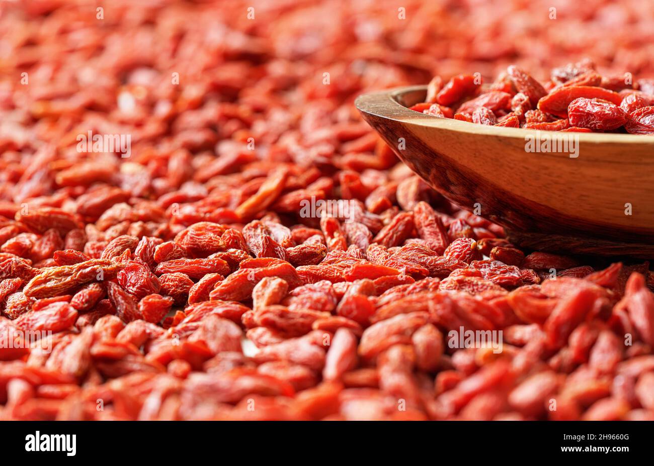 Trockene Goji-Beeren in einer kleinen Holzschüssel, verstreut auf dem Schreibtisch unten Stockfoto