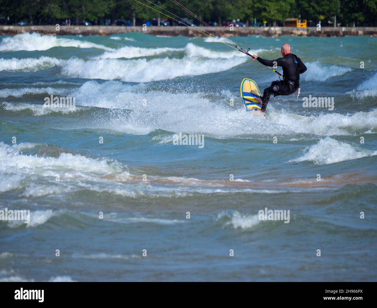 Ein Mann mittleren Alters kitesurft am Montrose Beach in Chicago. Beachten Sie, dass Sand durch eine Rissströmung im Vordergrund in den Lake Michigan gezogen wird. Stockfoto